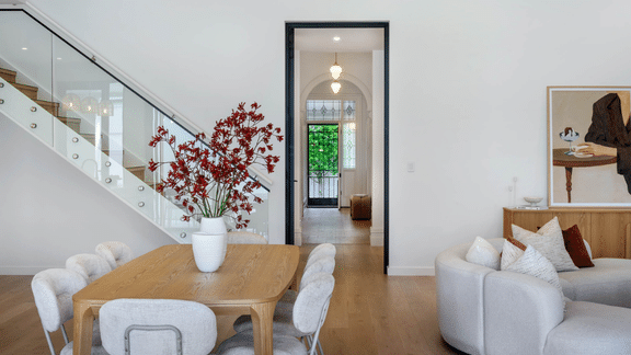 Luxury open-plan dining and living space with timber flooring, a glass staircase and preserved character details.