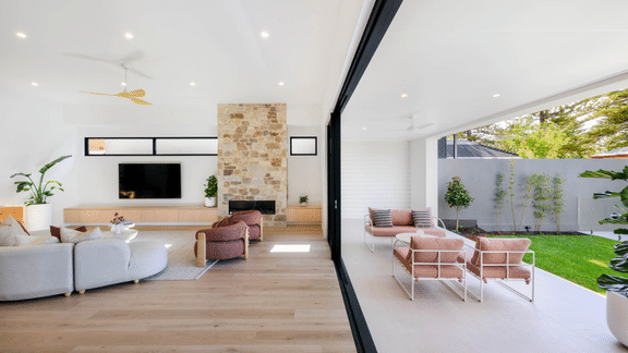 Light-filled open-plan living room with a stone fireplace and large glass doors opening to an alfresco area and garden.
